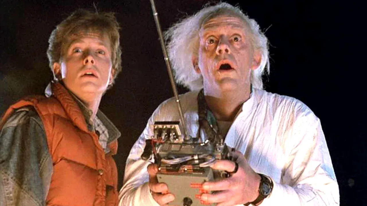 Christopher Lloyd como Doc Brown segura controle remoto e olha espantado para cima ao lado de Michael J. Fox como Marty McFly em De Volta para o Futuro.