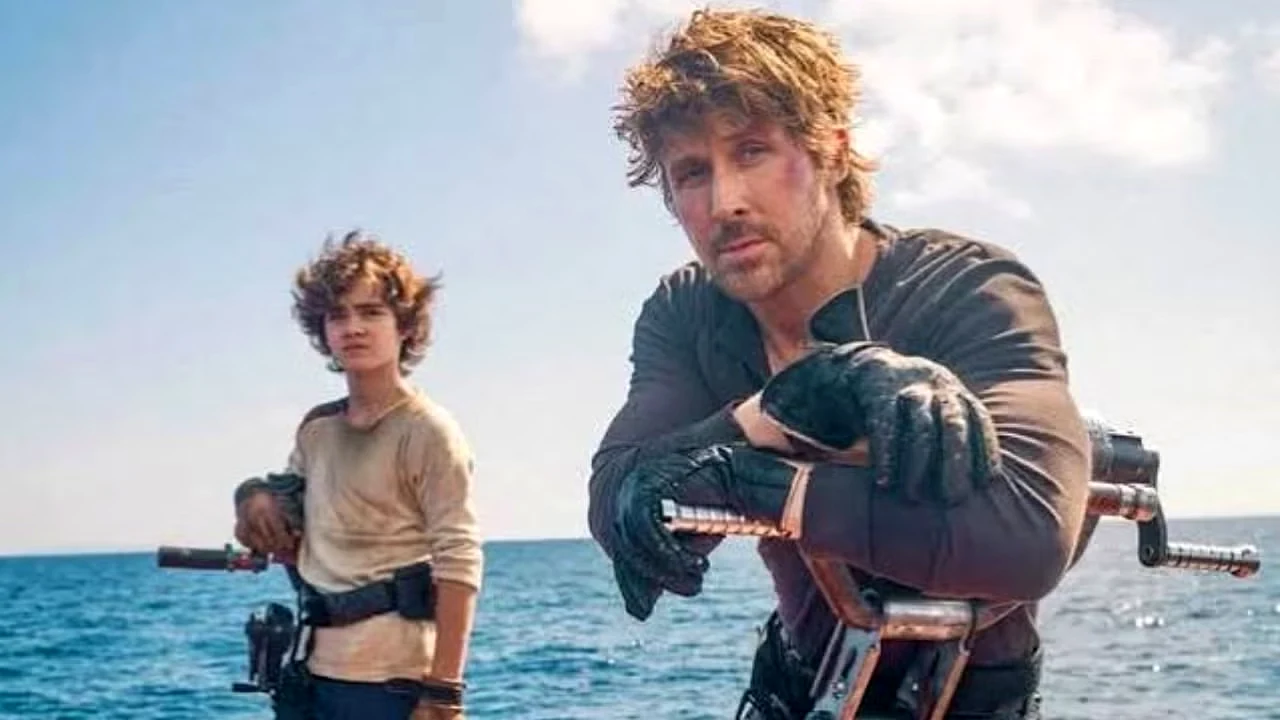 O ator Ryan Gosling com roupas rústicas apoiado em um veículo flutuante no mar, ao lado de um jovem ator em um cenário ensolarado.